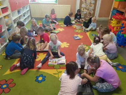 Dzieci siedzą na dywanie i oglądają książeczki.