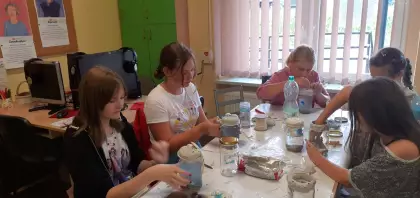 Dziewczyny wykonują morze w słoiku, sypiąc piasek i muszelki do naczynia szklanego. 