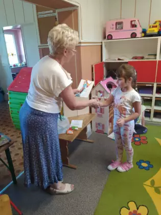 Pani bibliotekarka wręcza prezent na dzień przedszkolaka.