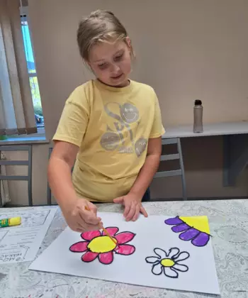 Dziewczyna maluje farbami obraz wyklejony włóczka.