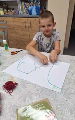 Chłopczyk przykleja kawałki włóczki do kartki papieru.