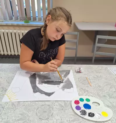 Dziewczyna maluje farbami obraz wyklejony włóczka.