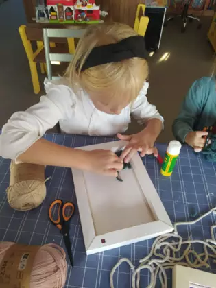 Dziewczynka wykleja obrazek kawałkami sznurka.