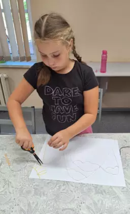 Dziewczyna przykleja kawałki włóczki do kartki papieru.