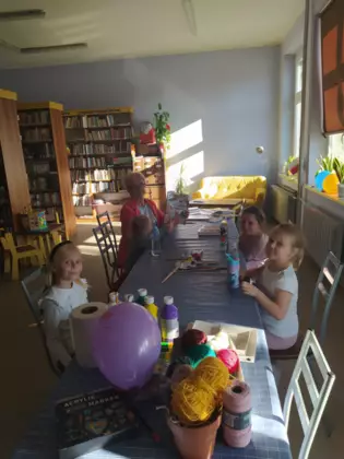 Dzieci siedzą przy stole i wykonują prace plastyczne.