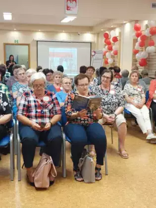 Seniorzy obecni na spotkaniu czytający książkę.