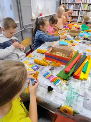 Dzieci przy stole wykonują kukurydziane ludziki.