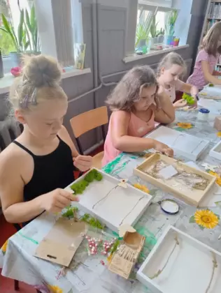 Dzieci przyozdabiają swoje ramki na zdjęcia mchem.