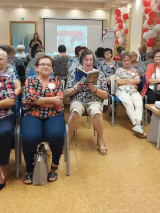 Seniorzy obecni na spotkaniu czytający książkę.