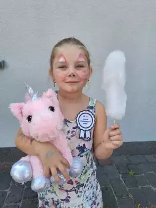 Dziewczynka z pomalowana buzia trzyma w ręce konika a w drugiej watę cukrowa.