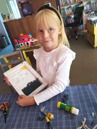 Dziewczynka wykleja obrazek kawałkami sznurka.