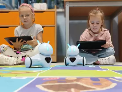 Dziewczynki trzymają w rękach tablety i kodują przejście dla robocików.