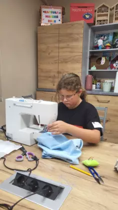 Dziewczynka siedzi przy maszynie i szyje spodenki.