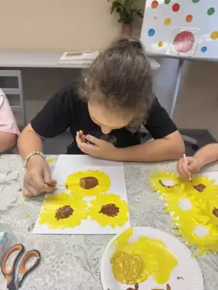 Dziewczynka maluje farbą słoneczniki.