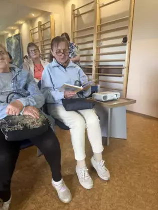 Uczestniczka spotkania czyta utwory Jana Kochanowskiego. W tle pozostali uczestnicy spotkania.