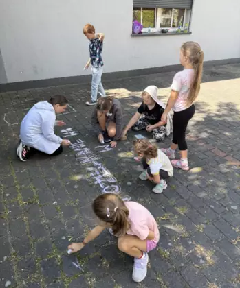 Dzieci malują kredami kolorowymi na chodniku.