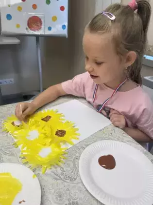 Dziewczynka patyczkiem kosmetycznym kropkuje środek słonecznika.