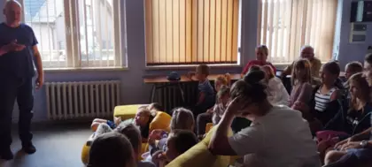 grupa dzieci siedzi i ogląda aktorów z marionetkami na scenie w bibliotece.