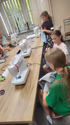 Troje dzieci siedzi przy maszynie i szyją spodenki.