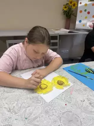 Dziewczynka patyczkiem kosmetycznym kropkuje środek pomalowanego żółta farbą słonecznika.