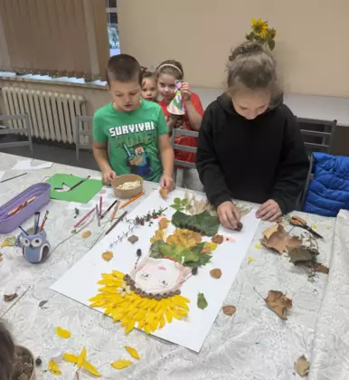 Uczestnicy zajęć tworzą barwną postać Pani Jesieni, wykorzystując naturalne materiały oraz kolorowy papier.