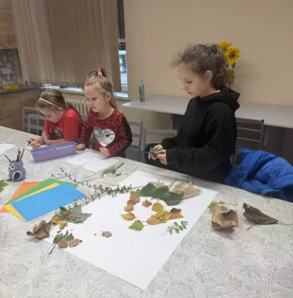 Uczestnicy zajęć zaczynają wspólną pracę nad postacią Pani Jesieni, układając materiały na dużym arkuszu.