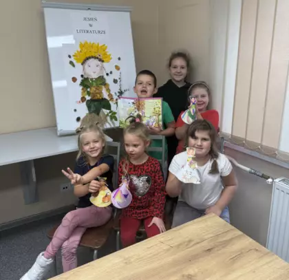 Wspólne zdjęcie uczestników przy Pani Jesieni; chłopiec trzyma w ręku książkę, podkreślając ideę głośnego czytania.