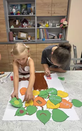 Dwie dziewczynki przyklejają liście lipy do drzewa.