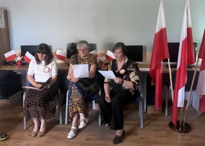 Trzy panie czytają fragmenty „Dziadów” Adama Mickiewicza, a obok nich znajduje się flaga Rzeczypospolitej Polskiej.
