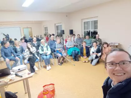 Grupa osób siedzi na krzesłach w sali sportowej. Siostra zakonna w okularach uśmiecha się.