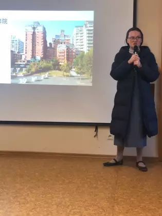 Siostra zakonna stoi przy dużym ekranie. W rękach trzyma mikrofon. Na ekranie wyświetla się prezentacja z Tajwanu.