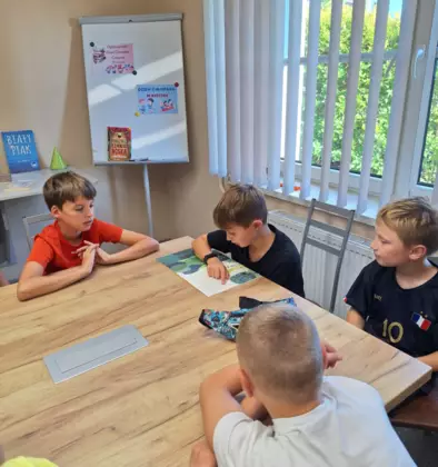 Chłopcy siedzą przy stole i słuchają opowiadania czytanego przez uczestnika zajęć.