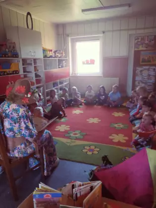 Pani bibliotekarka przebrana za Panią Jesień czyta dzieciom książeczkę.