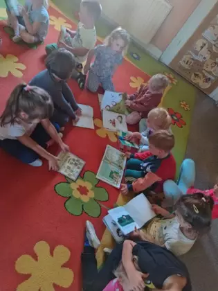 Przedszkolaki na dywanie oglądają książeczki.