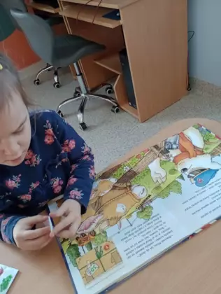 Dziewczynka ogląda książeczkę  pt. Miś listonosz. Na wsi.