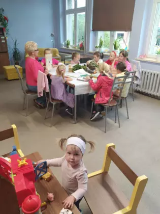 Dzieci siedzą przy stoliku i słuchają jak Pani z biblioteki czyta im książke.