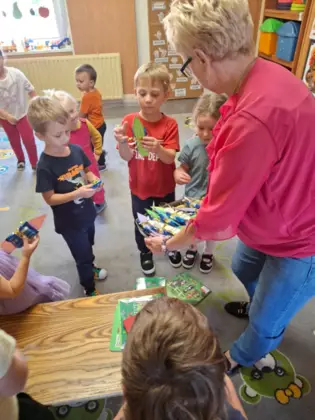 Pani z biblioteki rozdaje małe upominki dzieciom z przedszkola.