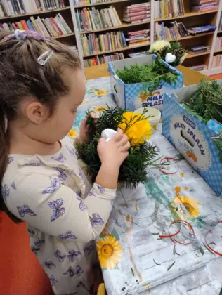 Dziewczynka wkłada jodłowe gałązki do stroika.