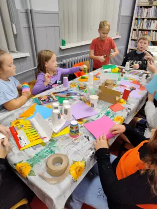 Dzieci przy wspólnym stoliku wykonują prace plastyczne z papierowych kubeczków.