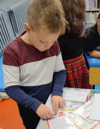 Chłopczyk nakleja znaczek na kopertę.