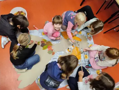 Dzieci kleją liśćmi Panią Jesień.