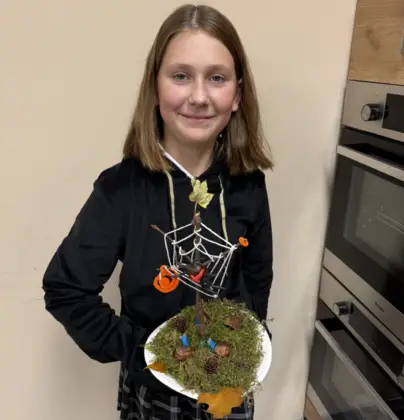 Uśmiechnięta dziewczynka prezentuje swoją pracę jesienne drzewko.