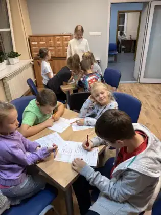 Dzieci siedzą przy stolikach i rozwiązują rysopisy, ćwicząc spostrzegawczość i detektywistyczne umiejętności.