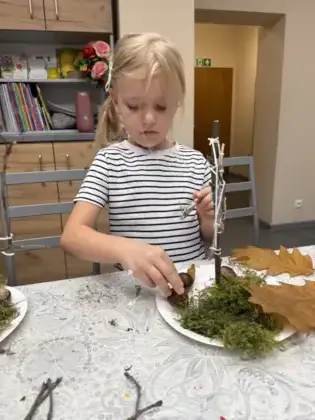 Dziewczynka przykleja kasztany pod swoim jesiennym drzewem.