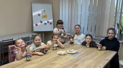 Dziewczynki siedzą przy stole z przygotowanymi słoiczkami musu i upieczonymi rogalikami.