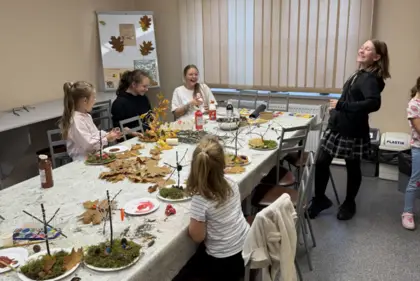 Pięć uśmiechniętych dziewczynek pracuje przy stole nad swoimi jesiennymi projektami, a na stole leżą kolorowe liście, kasztany i żołędzie