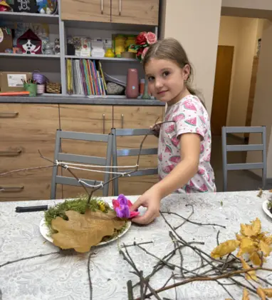 Uśmiechnięta dziewczynka przykleja kolorowy kwiat do swojego drzewka.