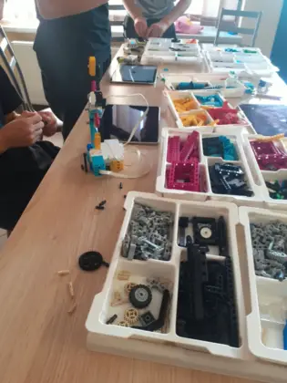 Na stoliku w pudełkach leżą klocki lego obok tablet i zbudowana konstrukcja.