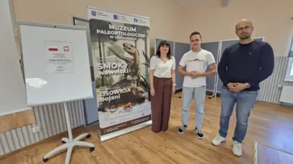 Dyrektor Gminnej Biblioteki w Pawonkowie oraz dwaj geolodzy stoją obok roll-upu z wizerunkiem smoka i lisowicji oraz napisem „Muzeum Paleontologiczne w Lisowicach”, a obok widoczna jest tablica z plakatem projektu „Galaktyka możliwości: przystanek Ziemia”.