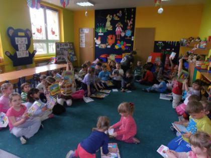 Przedszkolaki siedzą na dywanie i oglądają książeczki.